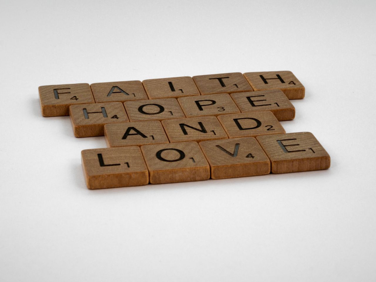 services-02 Wooden Scrabble tiles arranged to spell Faith, Hope, and Love against a white background.